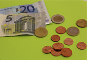Verschiedene Münzen und zwei Geldscheine liegen auf einer grünen Oberfläche.